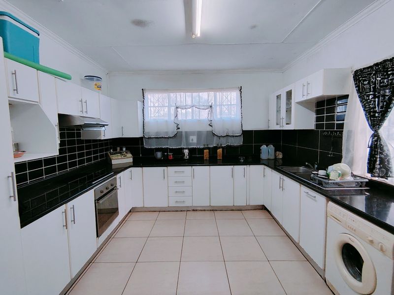 A functional U-shaped kitchen featuring white cabinetry, black tiled backsplash, dark granite countertops, and integrated stainless steel appliances.