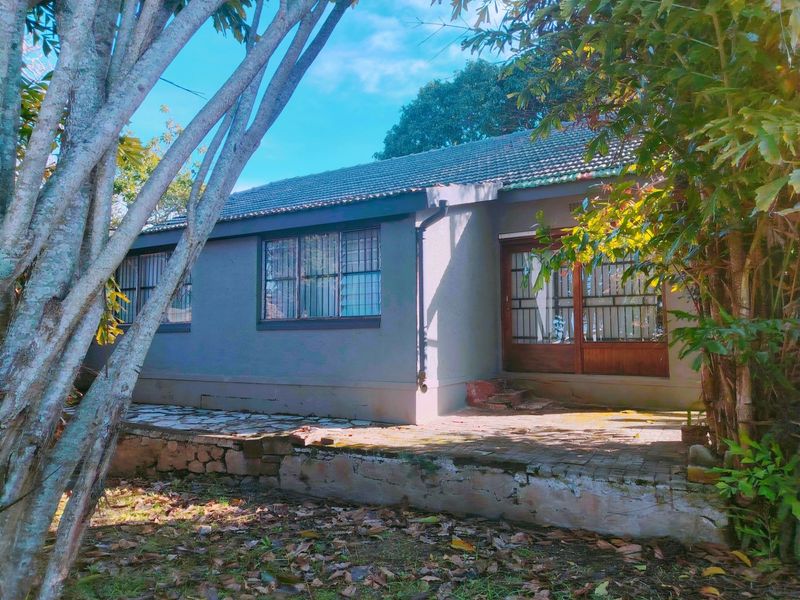 Rear view of the house featuring a tiled roof, security-barred windows, and a stone patio area requiring maintenance.