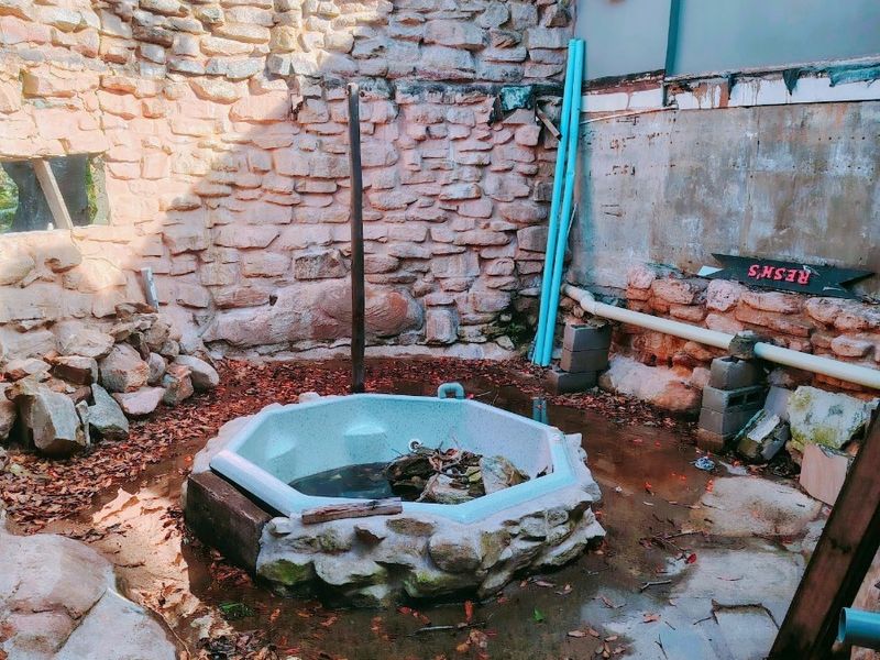 An outdoor area featuring a stone-walled enclosure and a built-in spa, currently in a state of significant disrepair and requiring extensive renovation.