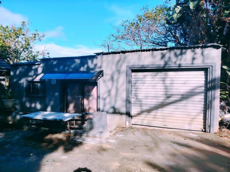 Exterior view of a detached garage featuring a roller shutter door, concrete driveway, and a small protective awning over the side entrance.