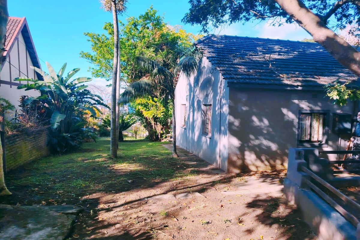A view of the rear exterior of the house featuring a tiled roof, security bars on windows, and a surrounding garden area.