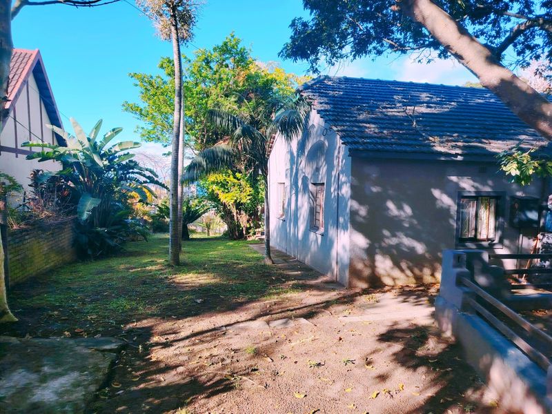 A view of the rear exterior of the house featuring a tiled roof, security bars on windows, and a surrounding garden area.