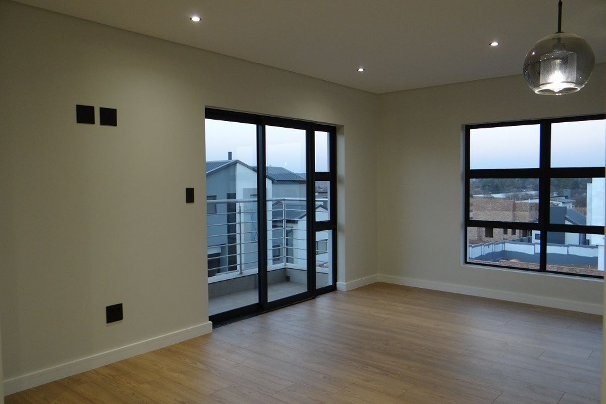 A bright, modern, and empty living room featuring laminate flooring, recessed downlights, and large aluminium-framed windows and sliding doors leading to a balcony.