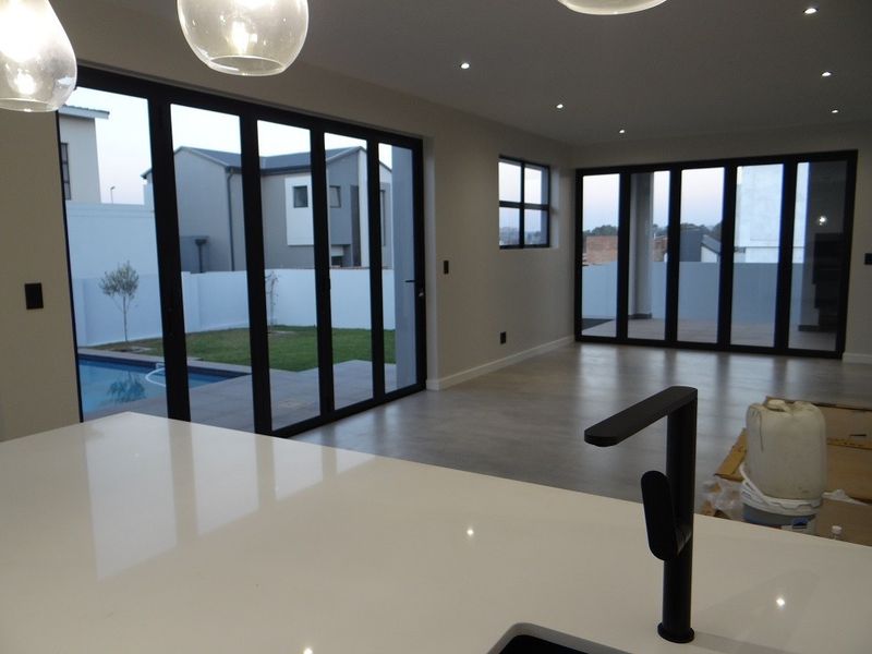 Spacious open-plan living area featuring modern finishes, large black aluminium stacker doors opening to the pool area, and a sleek kitchen island.