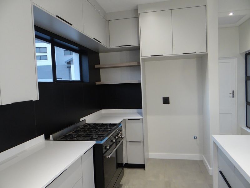Modern kitchen featuring sleek white cabinetry, contrasting black splashback, stone countertops, and a built-in gas stove with oven.