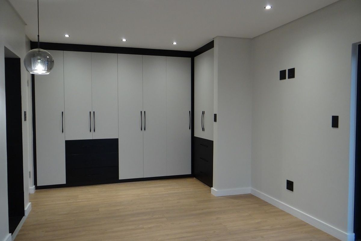 A modern, empty bedroom featuring sleek built-in cupboards with a two-tone finish, light wood-look laminate flooring, and recessed ceiling lighting.