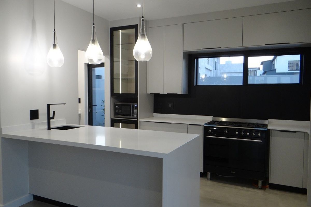 Modern kitchen featuring a central island with quartz countertops, sleek cabinetry, high-end black gas range, and contemporary pendant lighting.