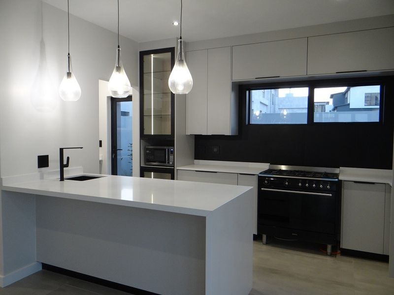 Modern kitchen featuring a central island with quartz countertops, sleek cabinetry, high-end black gas range, and contemporary pendant lighting.