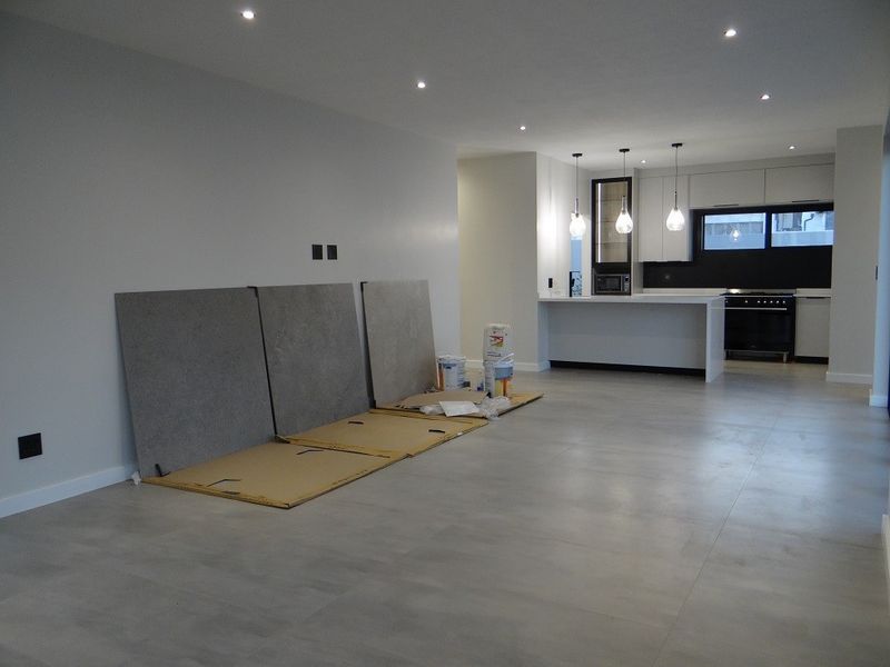 Modern open-plan living and kitchen area featuring sleek cabinetry, a central island, recessed lighting, and large format floor tiles in a neutral palette.