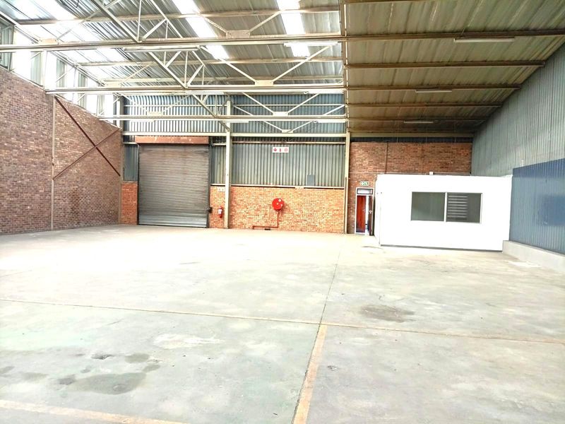 Spacious industrial warehouse unit featuring high ceilings with skylights, concrete flooring, a roller shutter door, and an integrated internal office structure.