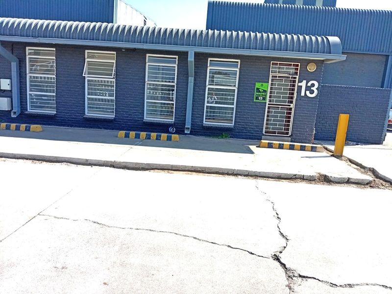 Front exterior view of a commercial unit featuring a dark blue brick facade, security-barred windows, and a concrete driveway with parking bollards.