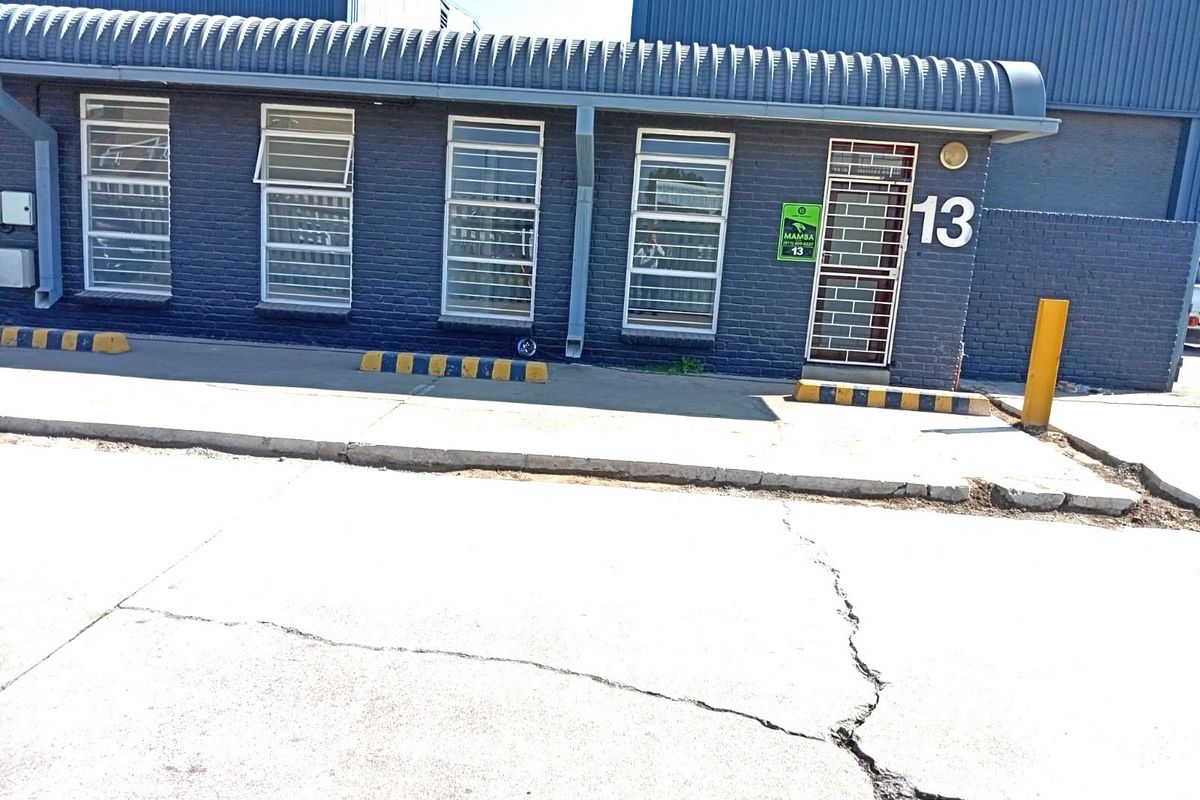 Front exterior view of a commercial unit featuring a dark blue brick facade, security-barred windows, and a concrete driveway with parking bollards.