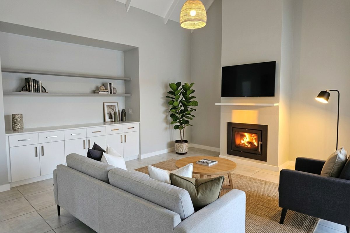 A bright living room featuring a vaulted ceiling, tiled flooring, built-in cabinetry with shelving, and a modern fireplace.