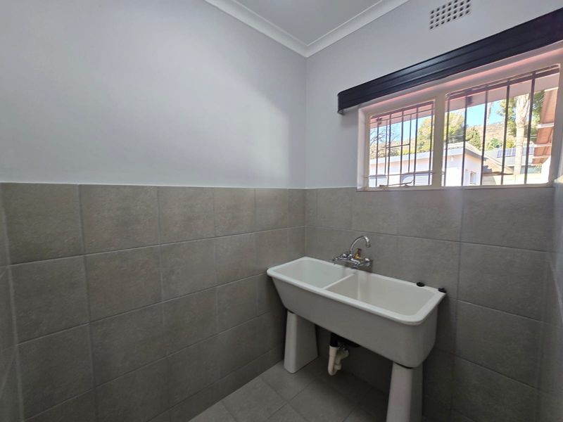 A clean and functional laundry area featuring a double utility sink, neutral wall tiling, and a window with security bars.