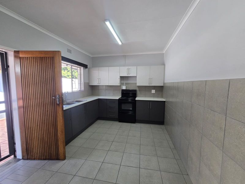 A clean, functional kitchen featuring dark lower cabinets, white upper cabinetry, tiled splashbacks, and tiled flooring, providing a neutral base for updates.