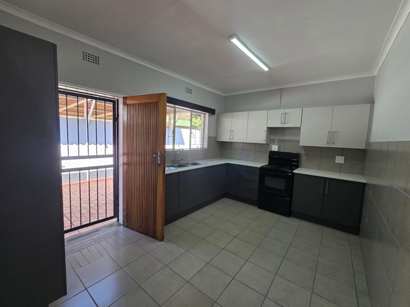 A clean, functional kitchen featuring two-tone cabinetry, tiled flooring, and direct access to an outdoor area through a security gate.