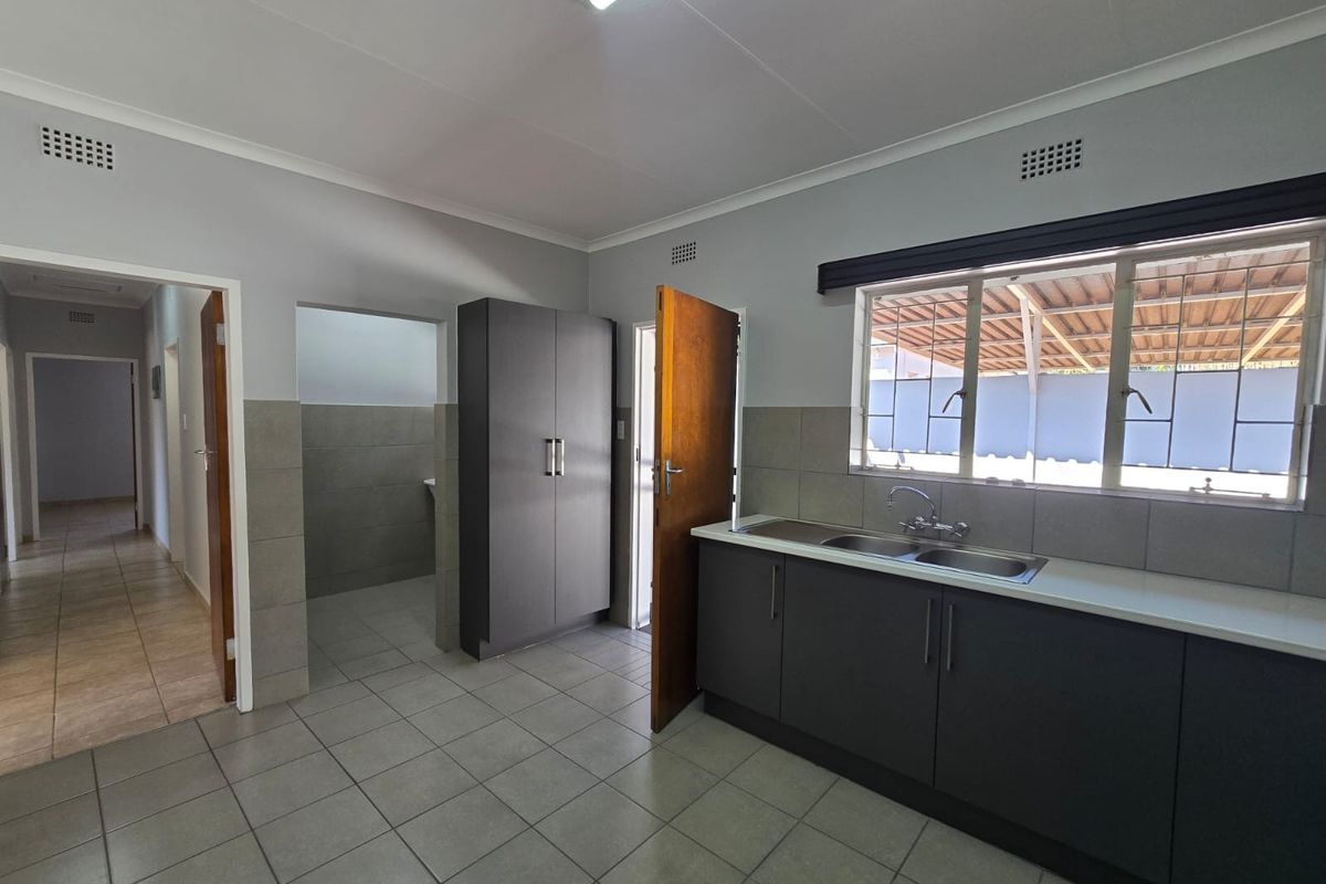 A clean, functional kitchen featuring dark grey cabinetry, a double stainless steel sink, tiled flooring, and a built-in pantry cupboard.