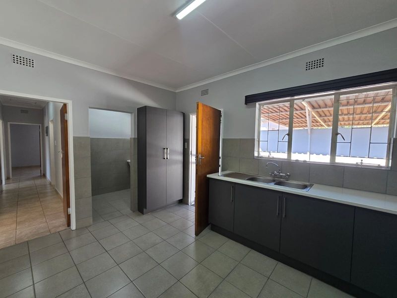 A clean, functional kitchen featuring dark grey cabinetry, a double stainless steel sink, tiled flooring, and a built-in pantry cupboard.