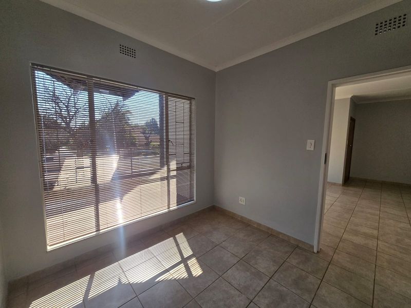 A bright, empty bedroom featuring neutral grey walls, tiled flooring, and fitted venetian blinds, offering a clean and versatile space.