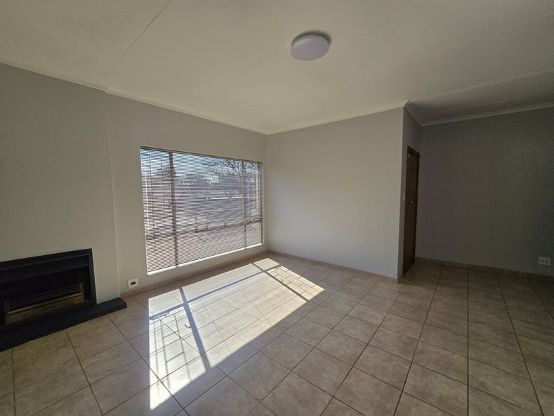 A bright, empty living room featuring tiled flooring, a built-in fireplace, and large windows with venetian blinds.