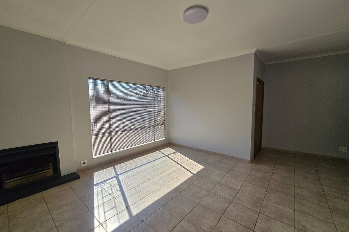 A bright, empty living room featuring tiled flooring, a built-in fireplace, and large windows with venetian blinds.