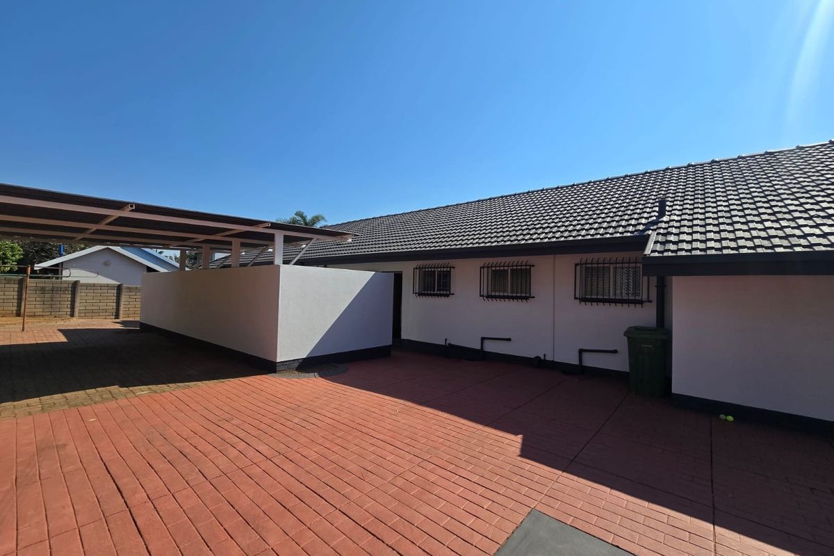 Rear exterior view of the property featuring a paved courtyard, a covered carport, and a well-maintained tiled roof structure.