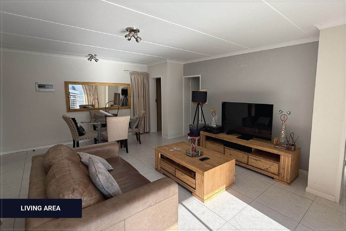 A well-lit living room featuring neutral tiled flooring and ceiling-mounted spotlights, offering a functional and comfortable space for relaxation.