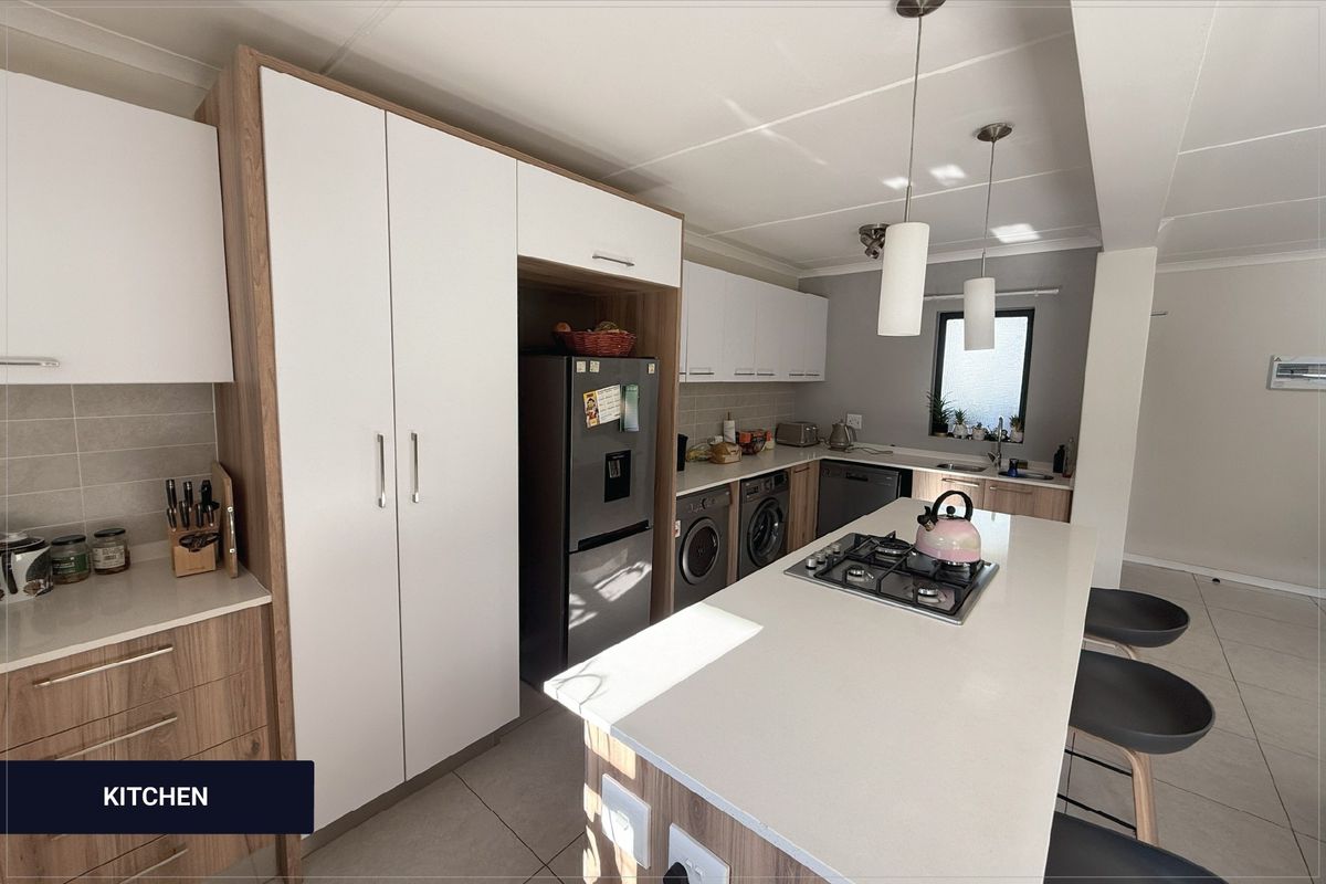Modern kitchen featuring two-tone cabinetry, stone countertops, a central island with a gas hob, and integrated laundry appliances.