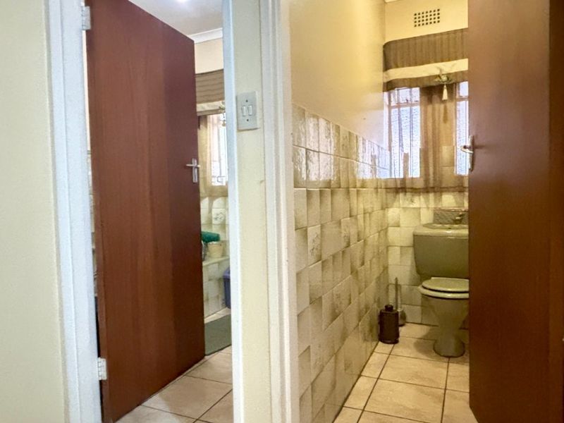 A hallway view showing access to a bathroom with tiled flooring, ceramic wall finishes, and a standard flush toilet.