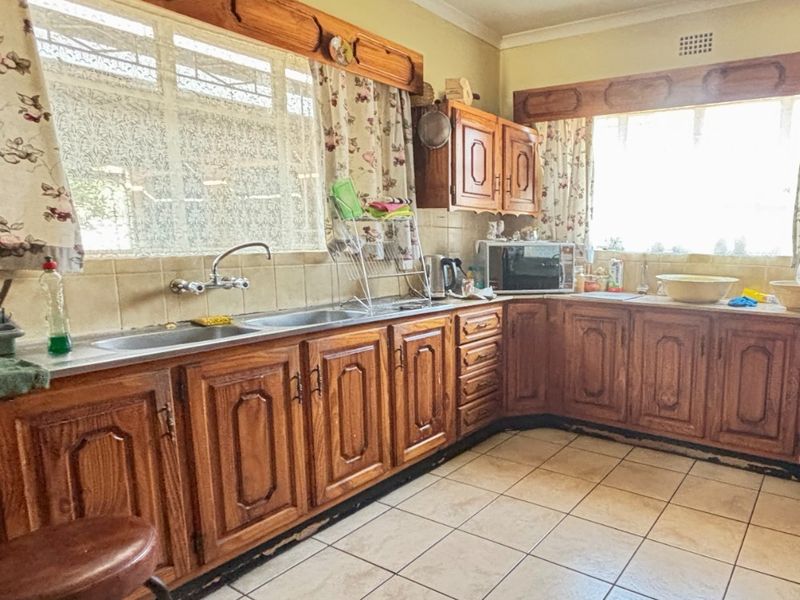 A dated kitchen featuring traditional wooden cabinetry, tiled flooring, and a double basin sink, offering significant potential for a modern renovation.