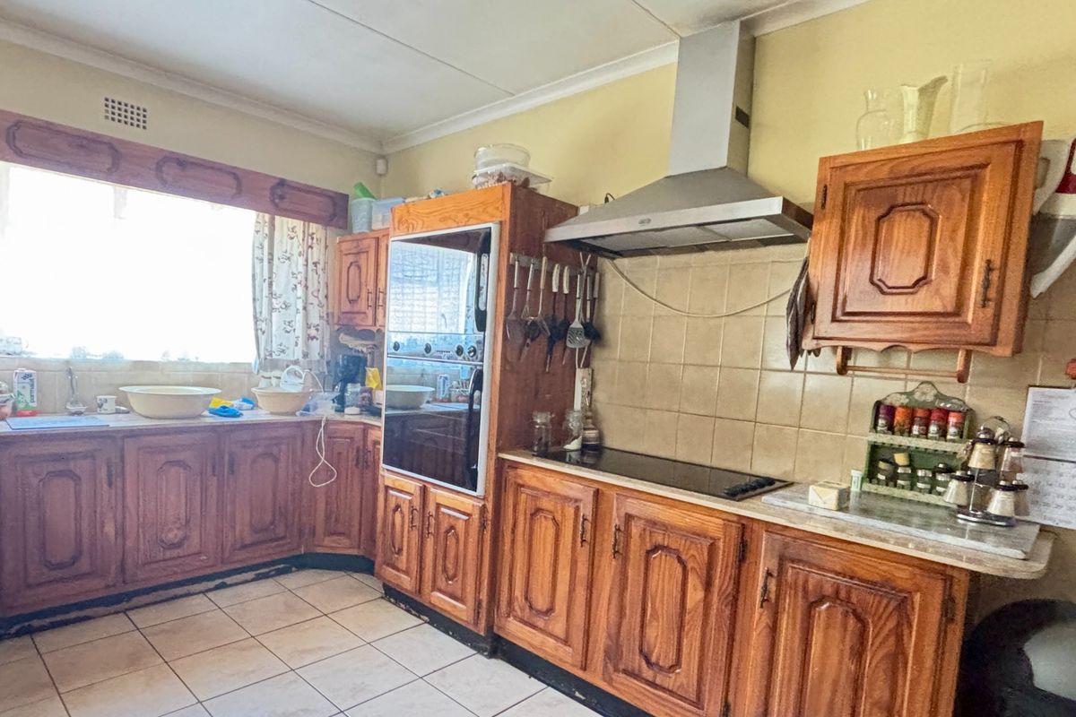 A functional kitchen featuring traditional wooden cabinetry, built-in oven, extractor fan, and tiled flooring, offering potential for a modern renovation.