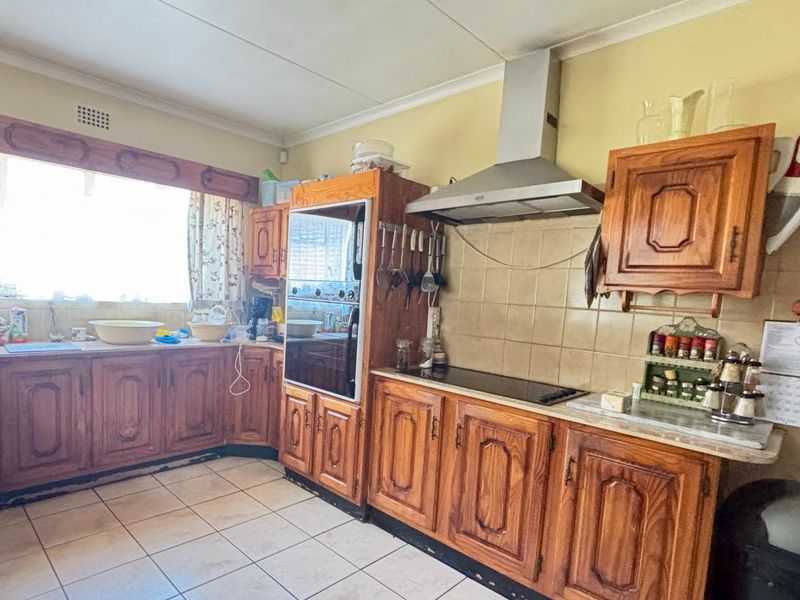 A functional kitchen featuring traditional wooden cabinetry, built-in oven, extractor fan, and tiled flooring, offering potential for a modern renovation.