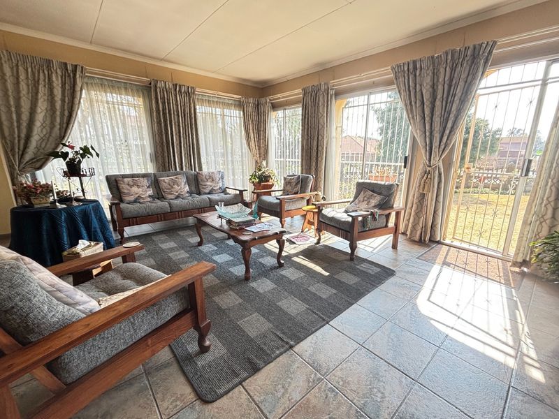 A sunlit living room featuring tiled flooring and large sliding glass doors with security gates, providing direct access to the outdoor area.