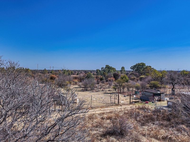 An aerial view of a vacant residential plot featuring dry vegetation, wire fencing, and small existing outbuildings.