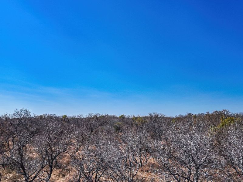 An aerial view of a vacant residential plot featuring natural bushveld vegetation under a clear blue sky.