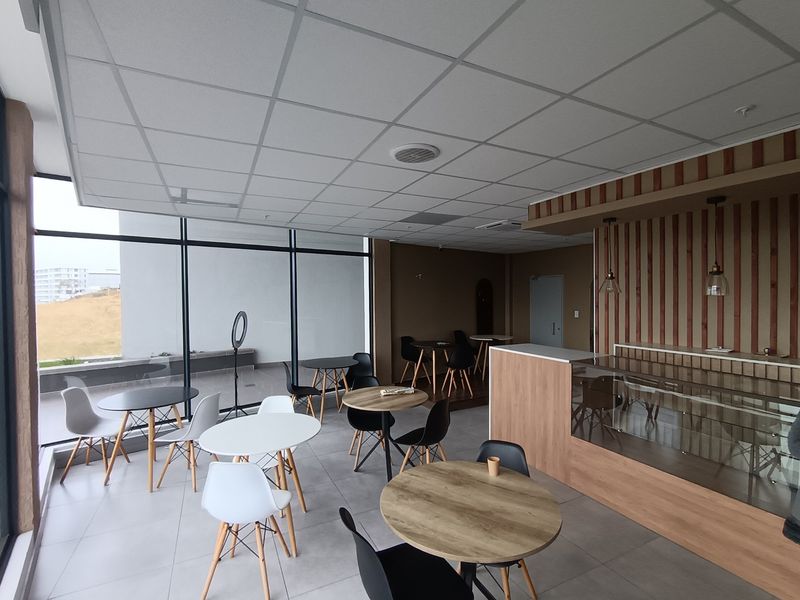 Open-plan retail or cafe space featuring large floor-to-ceiling windows, a built-in service counter, and modern tiled flooring with a suspended ceiling.