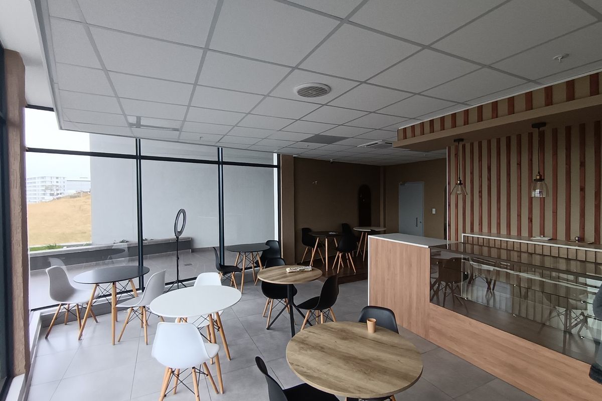 Open-plan retail or cafe space featuring large floor-to-ceiling windows, a built-in service counter, and modern tiled flooring with a suspended ceiling.