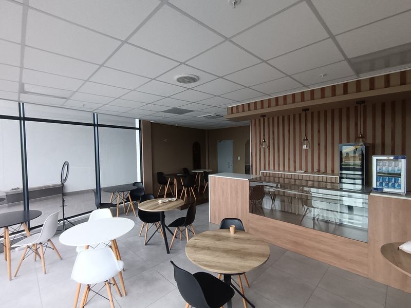 Modern retail or cafe space featuring a glass display counter, timber slat wall accents, suspended ceiling, and large storefront windows with tiled flooring.