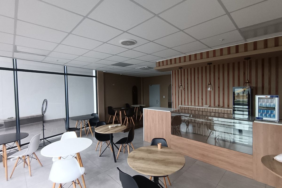 Modern retail or cafe space featuring a glass display counter, timber slat wall accents, suspended ceiling, and large storefront windows with tiled flooring.