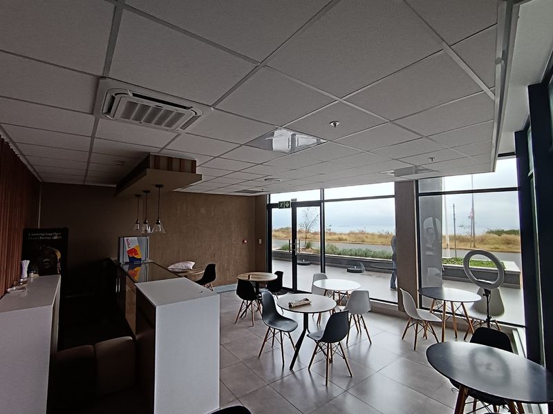 Modern open-plan retail or commercial space featuring large glass windows, tiled flooring, a suspended ceiling with integrated air conditioning, and a built-in service counter.