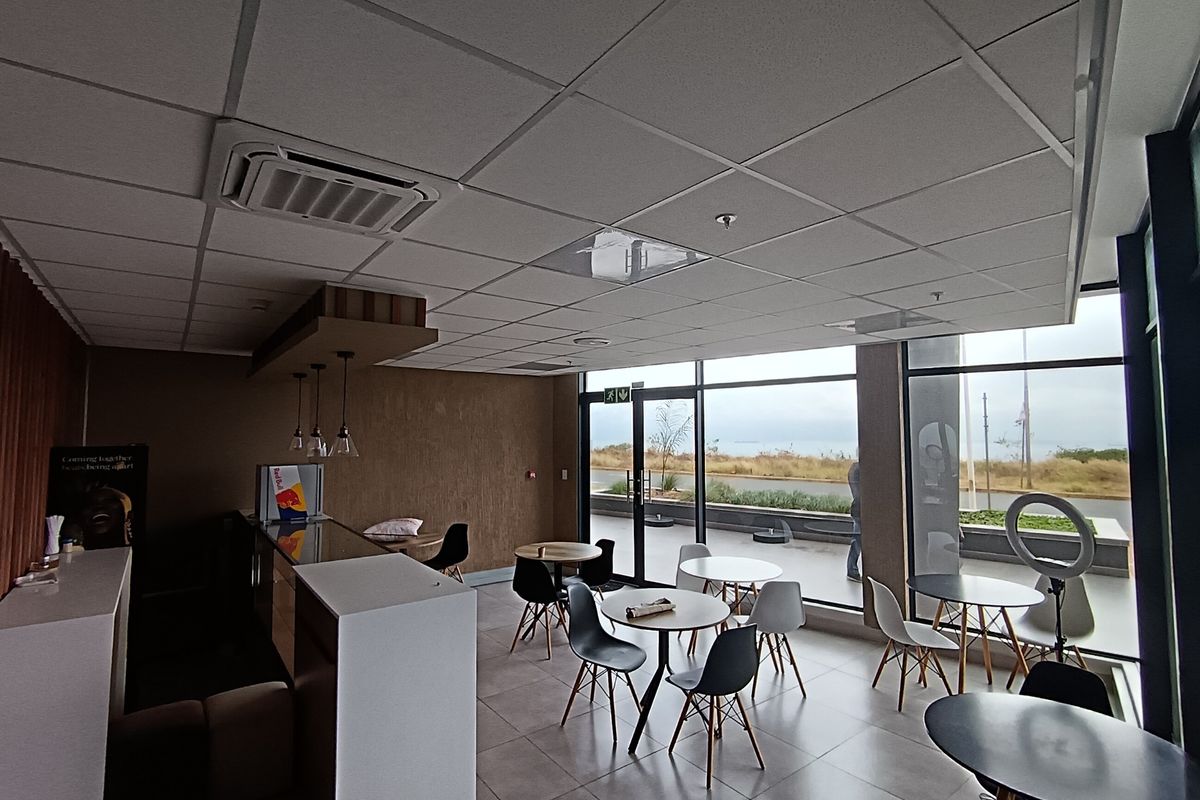 Modern open-plan retail or commercial space featuring large glass windows, tiled flooring, a suspended ceiling with integrated air conditioning, and a built-in service counter.