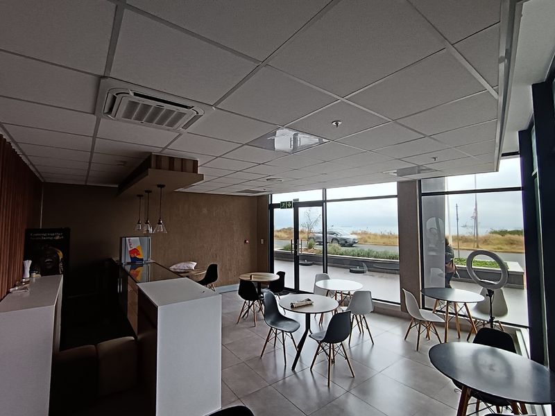Modern open-plan retail or cafe space featuring large glass windows, tiled flooring, and a suspended ceiling with integrated air conditioning.