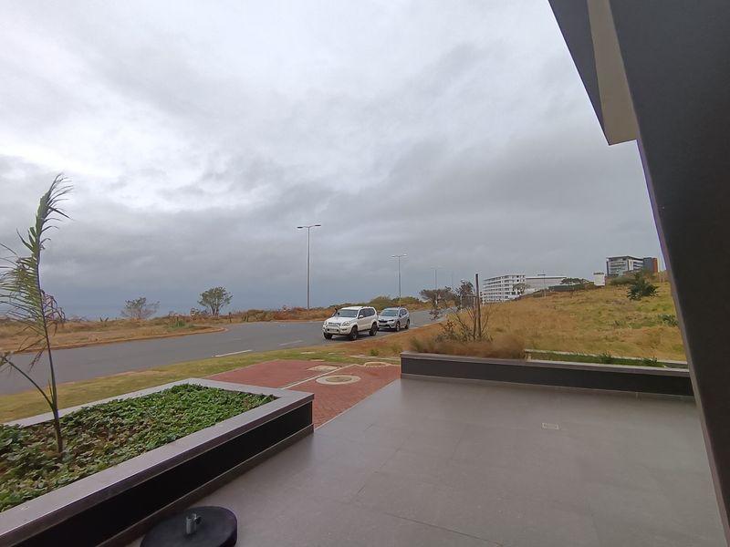 A covered outdoor patio area featuring tiled flooring and a built-in planter box, overlooking a street and surrounding landscape.