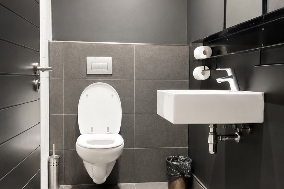 A modern, minimalist bathroom featuring dark grey wall and floor tiles, a wall-mounted toilet with concealed cistern, and a sleek wall-mounted basin.