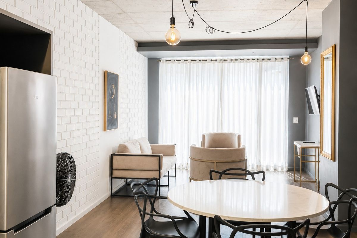 Modern open-plan living and dining area featuring an exposed concrete ceiling, white brick accent wall, and large sliding doors leading to natural light.
