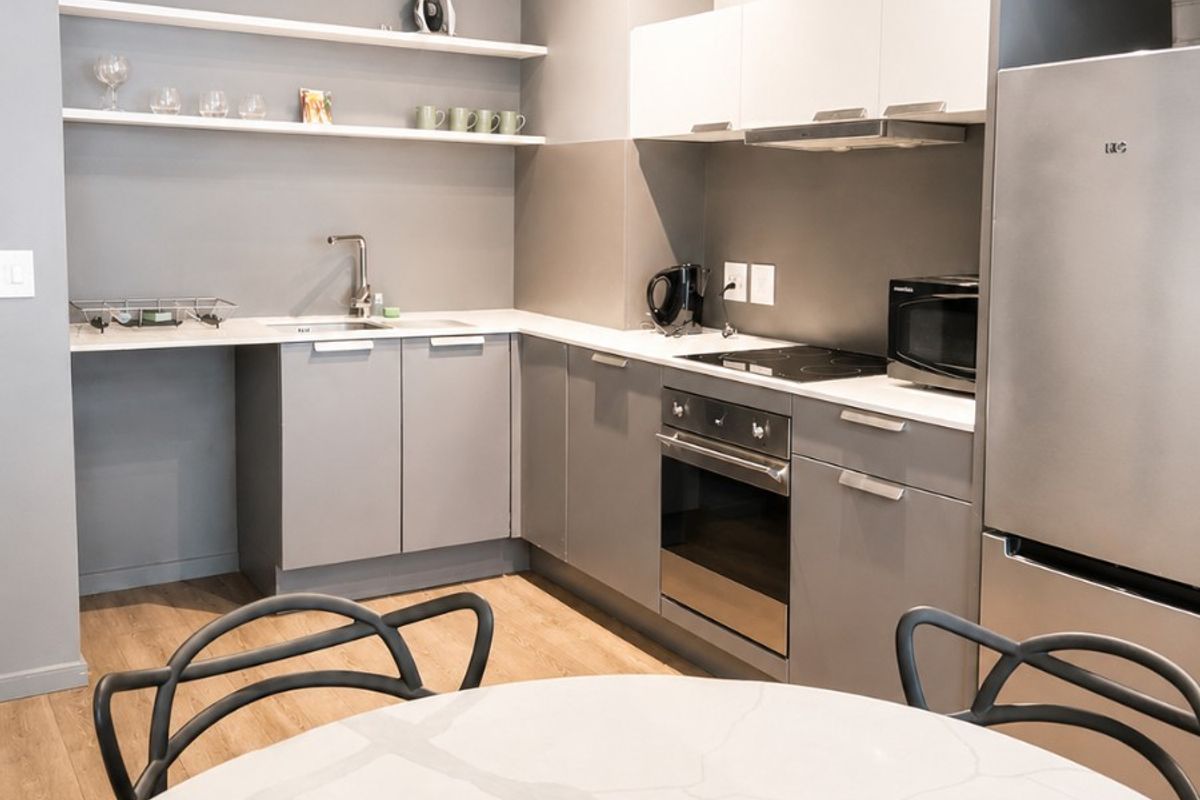 Modern open-plan kitchen featuring sleek grey cabinetry, stone-look countertops, subway tile backsplash, and industrial-style track lighting against an exposed concrete ceiling.