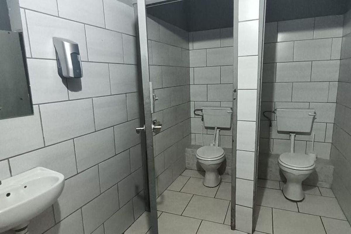 Commercial bathroom facility featuring dual toilet cubicles, tiled flooring, subway wall tiles, and a wall-mounted basin.