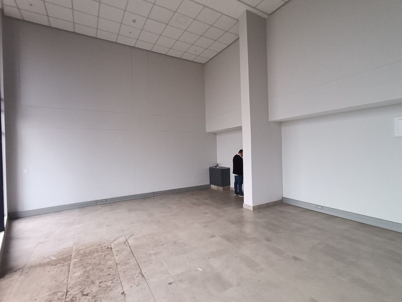 Spacious open-plan retail area featuring high ceilings, tiled flooring, and a compact built-in kitchenette unit.