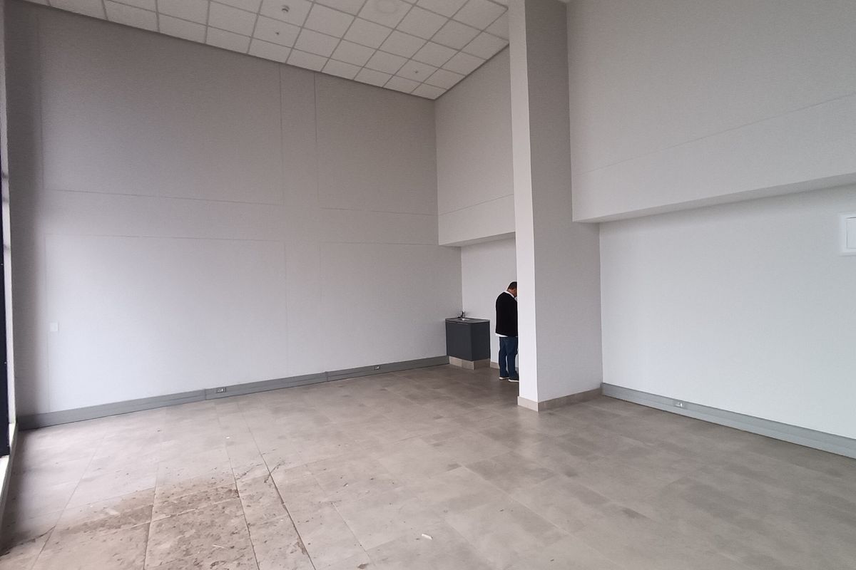 Spacious open-plan retail area featuring high ceilings, tiled flooring, and a compact built-in kitchenette unit.