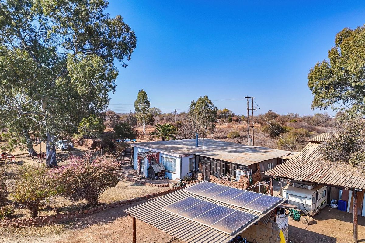 Aerial view of a farm property featuring a main dwelling with solar panels, corrugated roofing, and surrounding rural landscape.